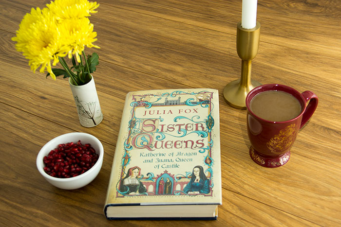 Sister Queens by Julia Fox. Book with a cup of coffee, pomegranate seeds, and flowers.